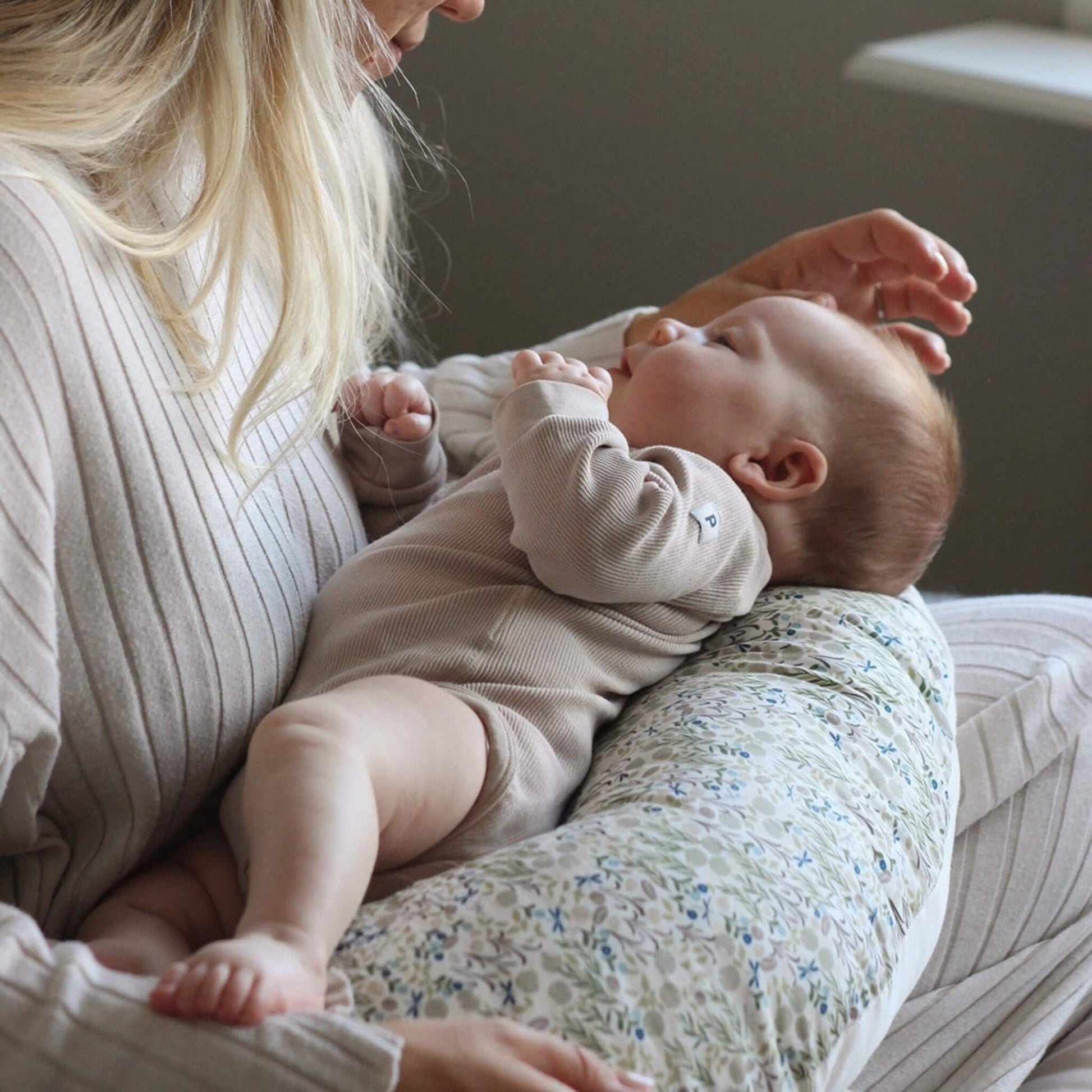 Woman holding a baby supported on a floral nursing pillow during feeding.