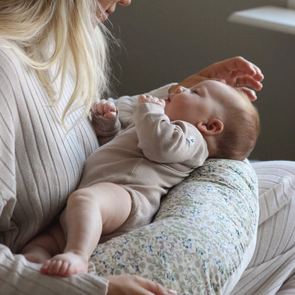 Woman holding a baby supported on a floral nursing pillow during feeding.