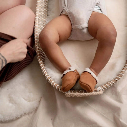 Baby wearing Baa Baby tan lambskin booties while lying in a Moses basket lined with soft sheepskin.