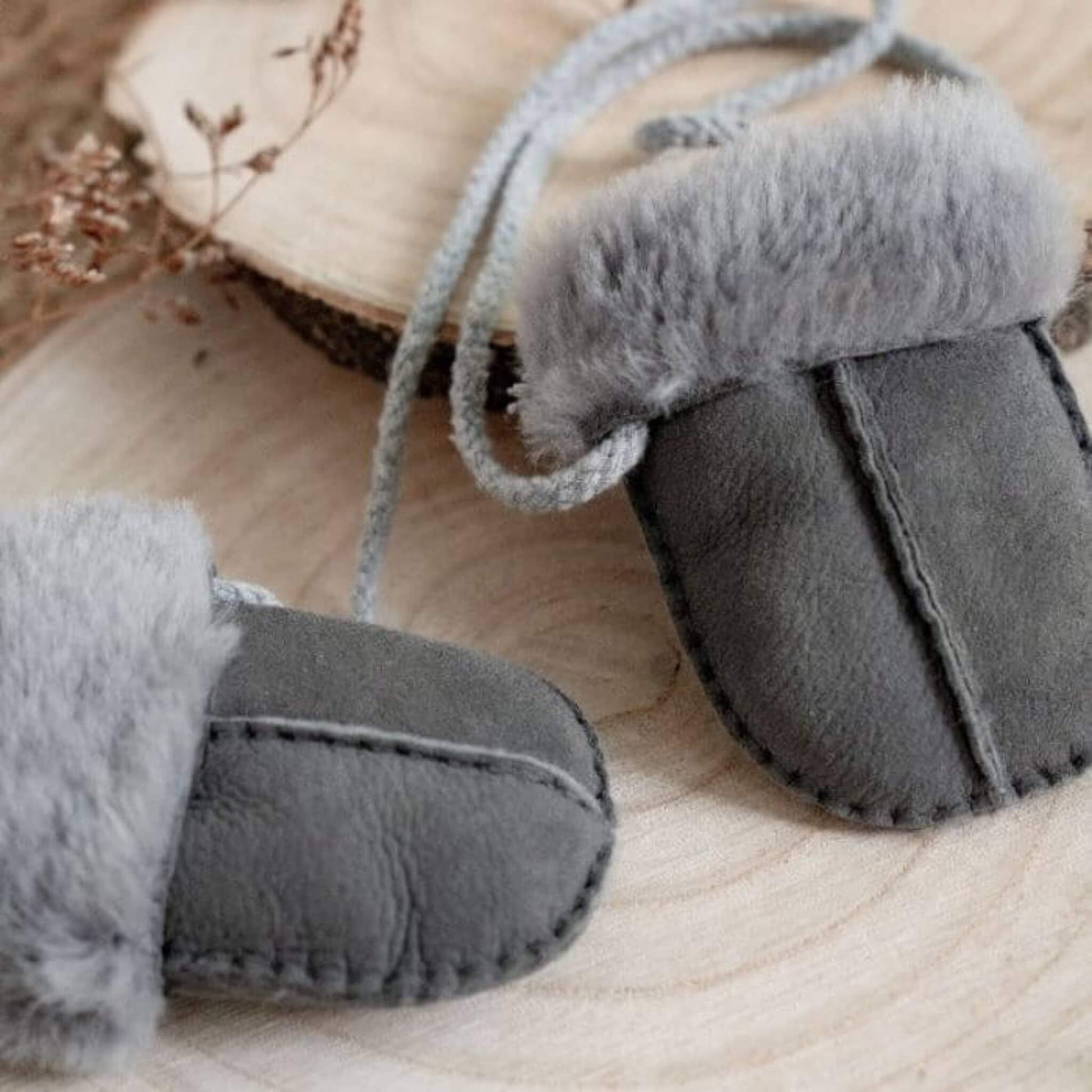 Close-up of Baa Baby grey sheepskin mittens on a wooden surface, showing fluffy lining and natural suede texture.