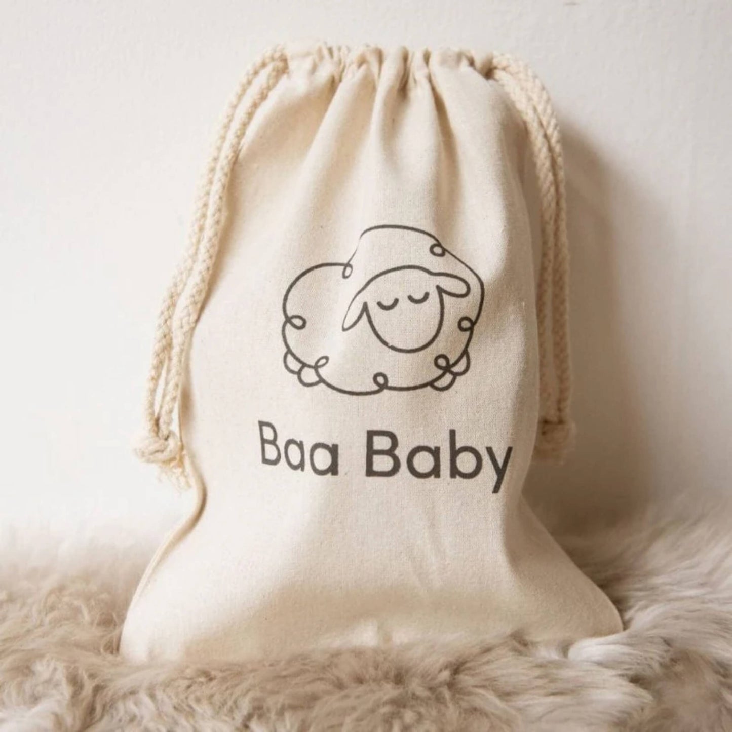 Baa Baby branded cotton drawstring bag resting on soft sheepskin, ideal for storing baby sheepskin accessories.