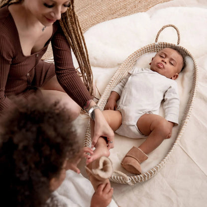 Mother and child dressing baby in Baa Baby sheepskin booties while lying in a basket lined with soft fleece.