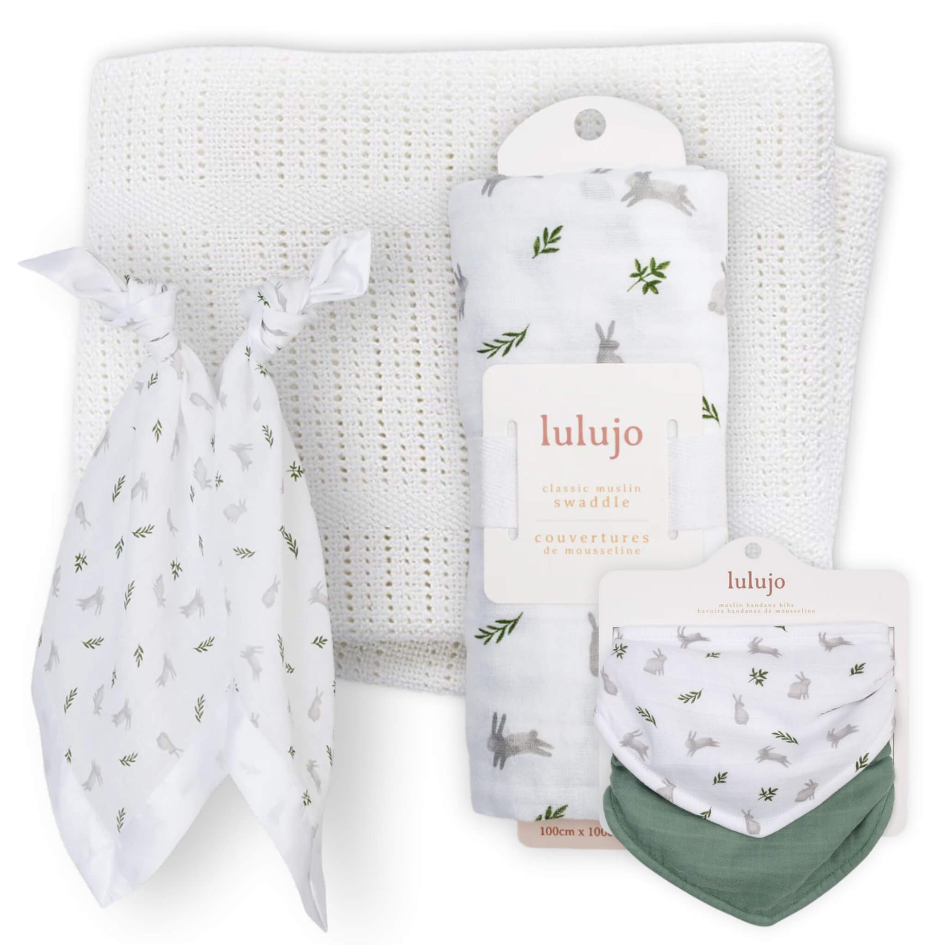 Coordinated baby gift set arranged together featuring a white knitted cellular blanket, a rolled white muslin swaddle with grey bunny and green leaf print, two matching knotted security blankets and a pack of two bandana bibs in bunny print and sage green.