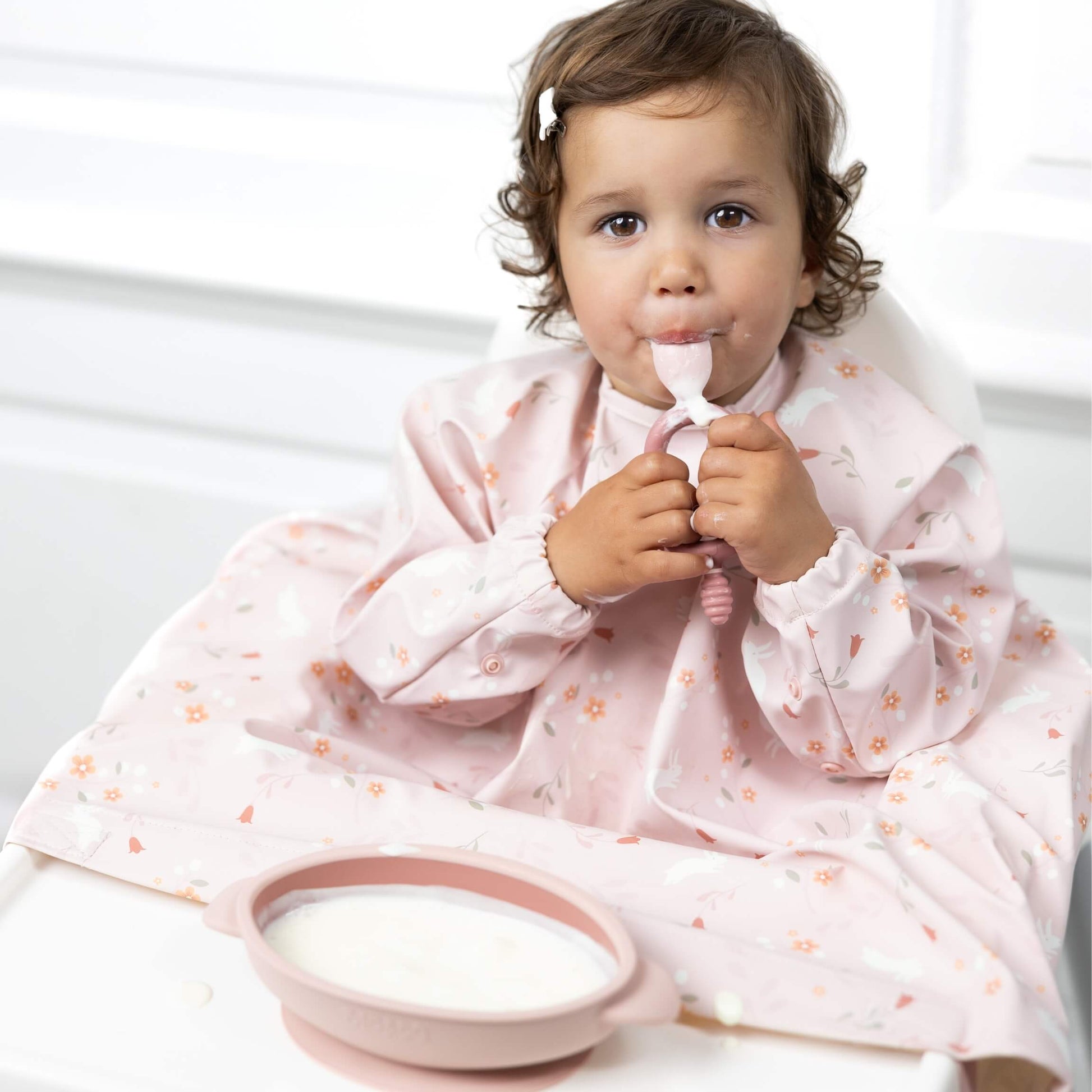 Toddler wearing the Botanical Bunnies Bibado bib while self-feeding with a spoon.