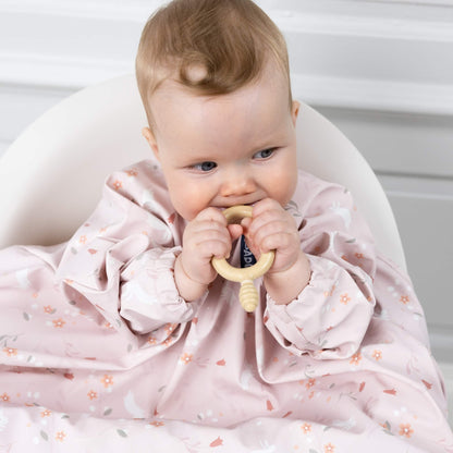 Baby wearing the coverall long sleeve weaning bib and holding a teether, showing sleeve coverage.