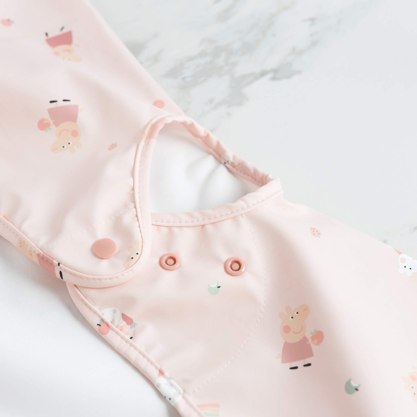 Neckline and popper fastening detail on the Peppa Pig bib, shown on a marble surface.