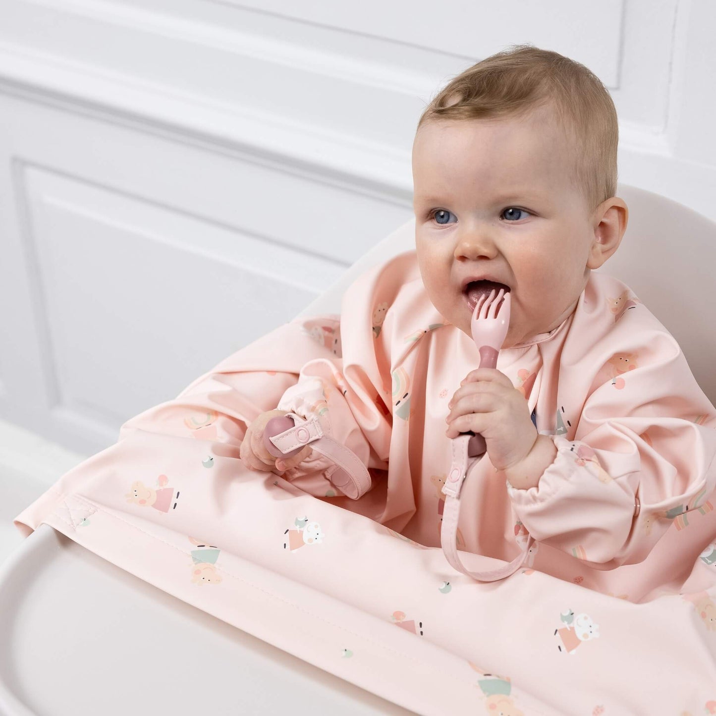Baby in Peppa Pig bib chewing a fork, attached to the sleeve with a matching strap.
