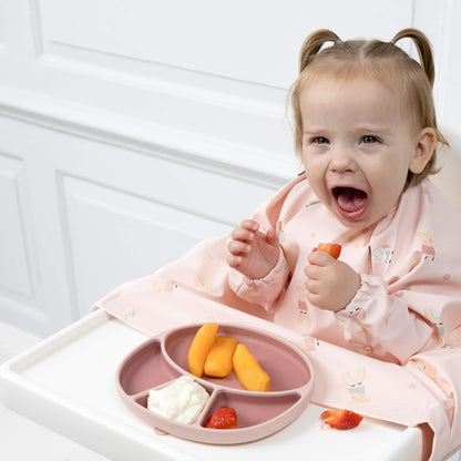 Toddler in Peppa Pig coverall bib smiling at mealtime, seated at highchair with food tray.
