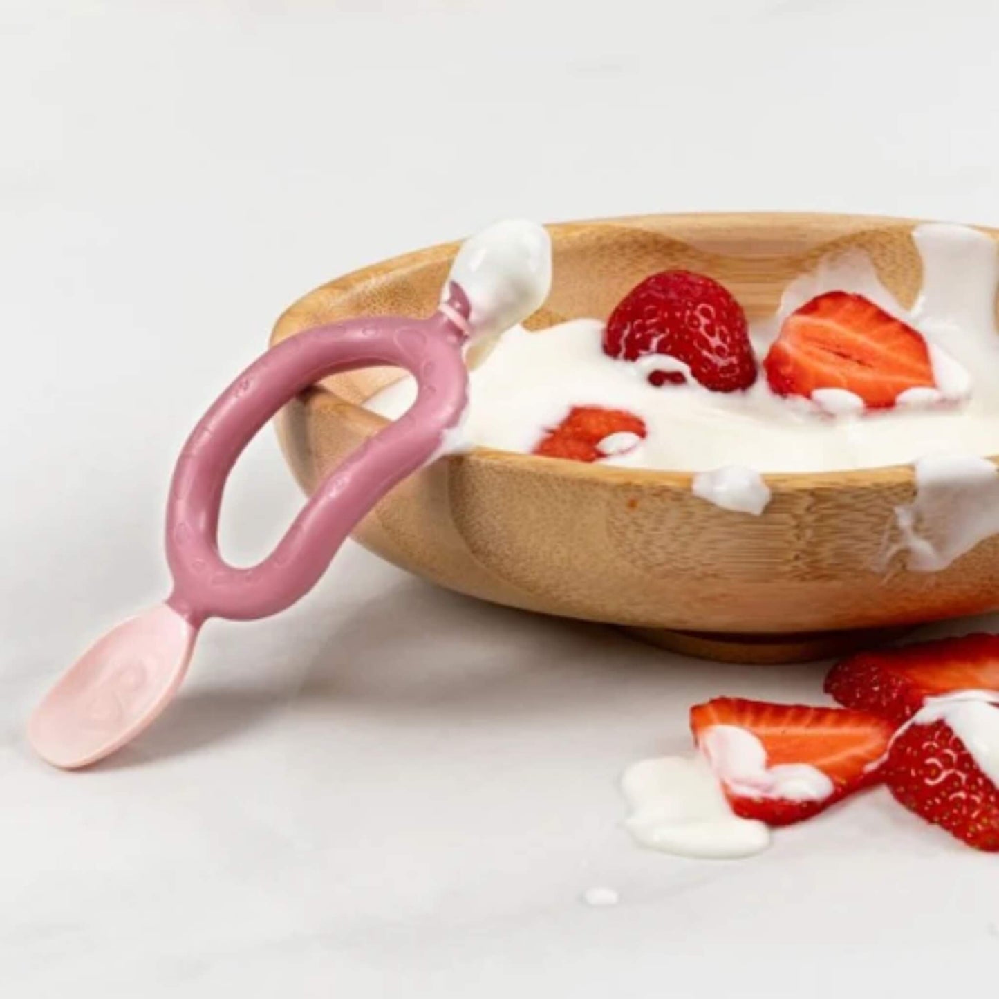 Bibado Dippit spoon resting on the edge of a wooden bowl filled with yoghurt and strawberries, showing food-friendly design.