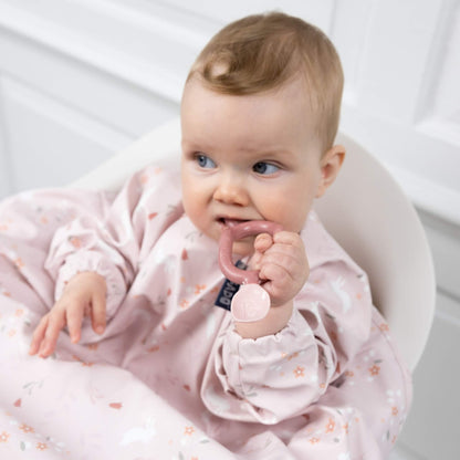 Baby in a highchair holding the blush pink Bibado Dippit spoon while chewing on one end during mealtime.