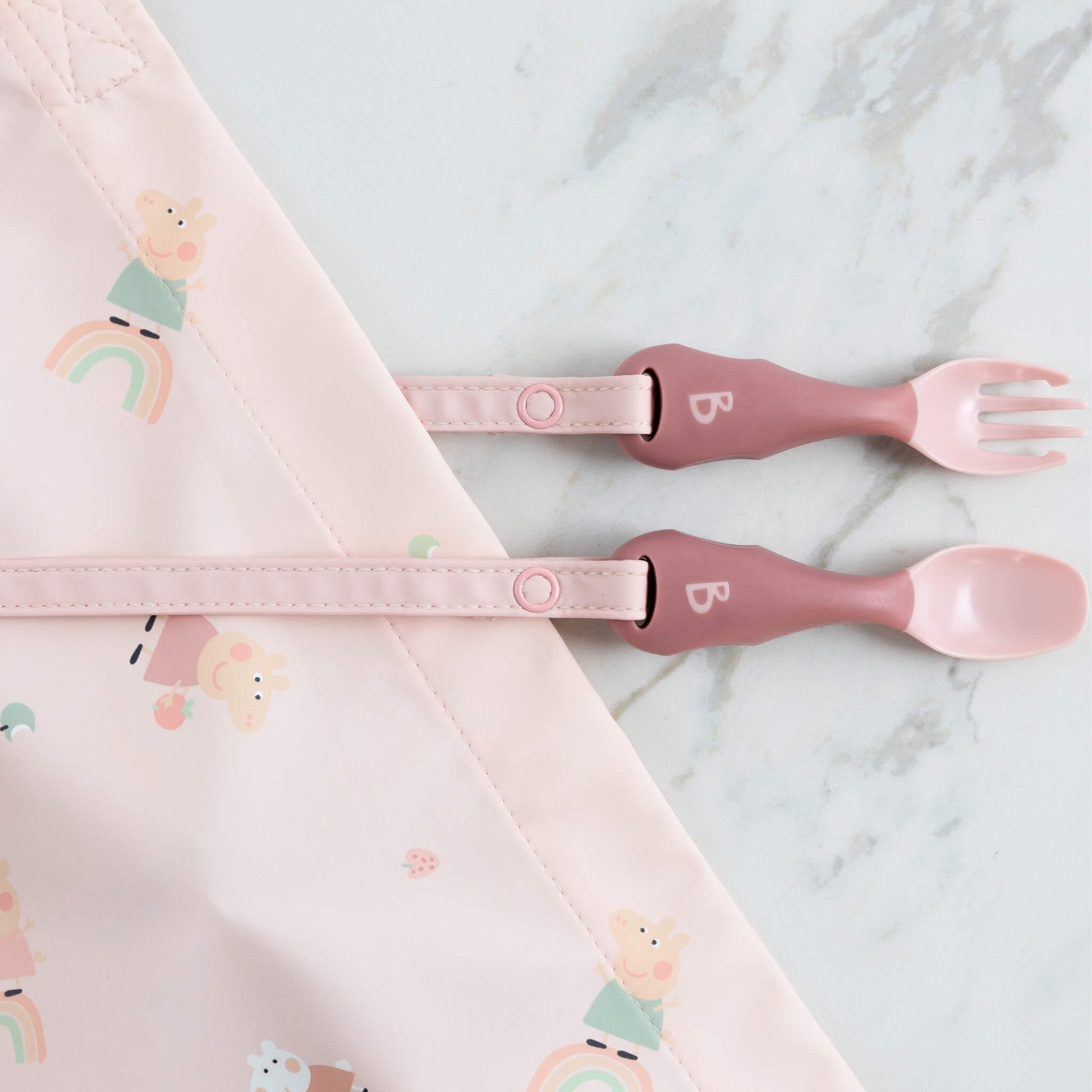 Cutlery attached to a Peppa Pig coverall bib with rainbow print, ready for baby-led weaning.