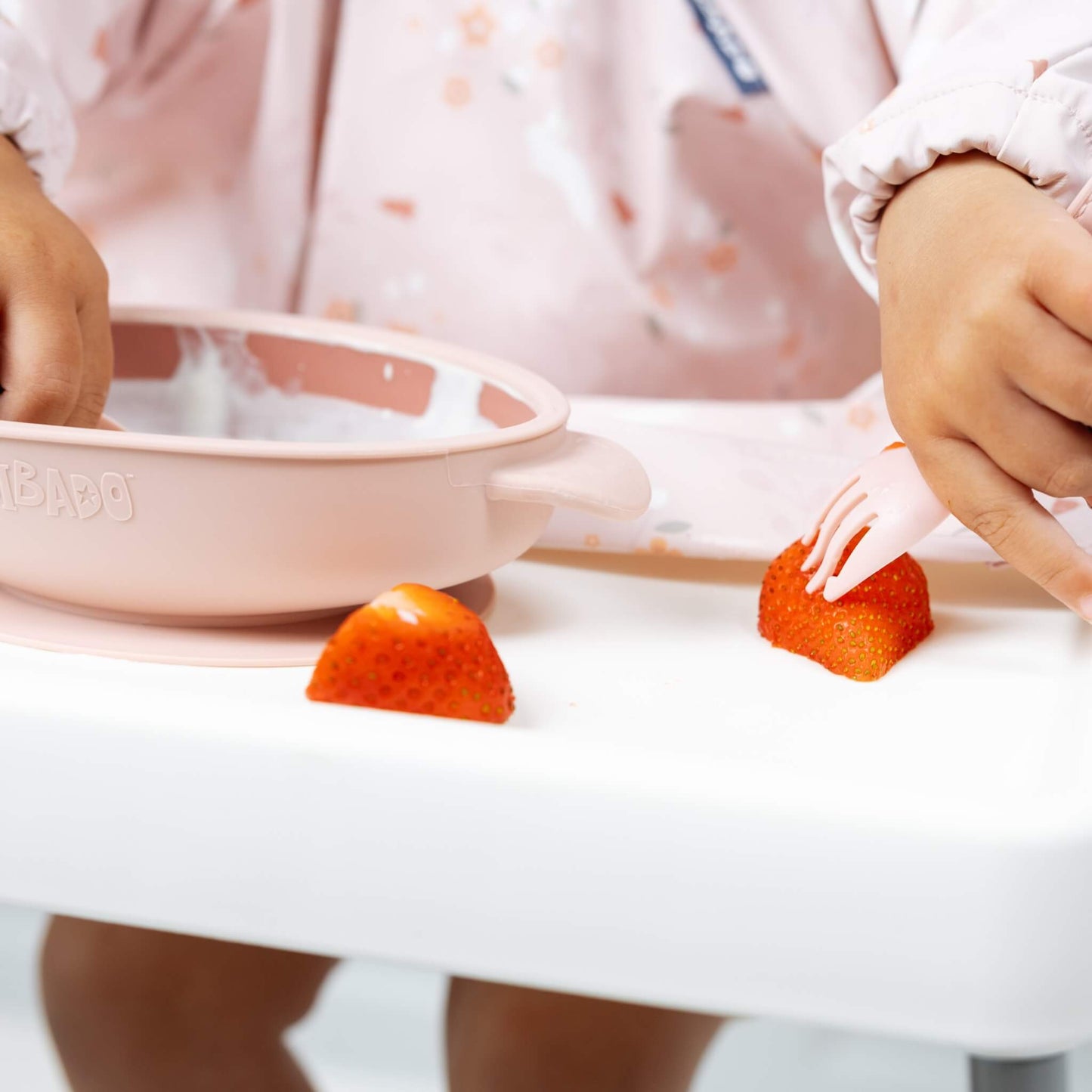 Weaning setup showing utensils attached to the sleeve ends of a waterproof bib using popper fastenings.