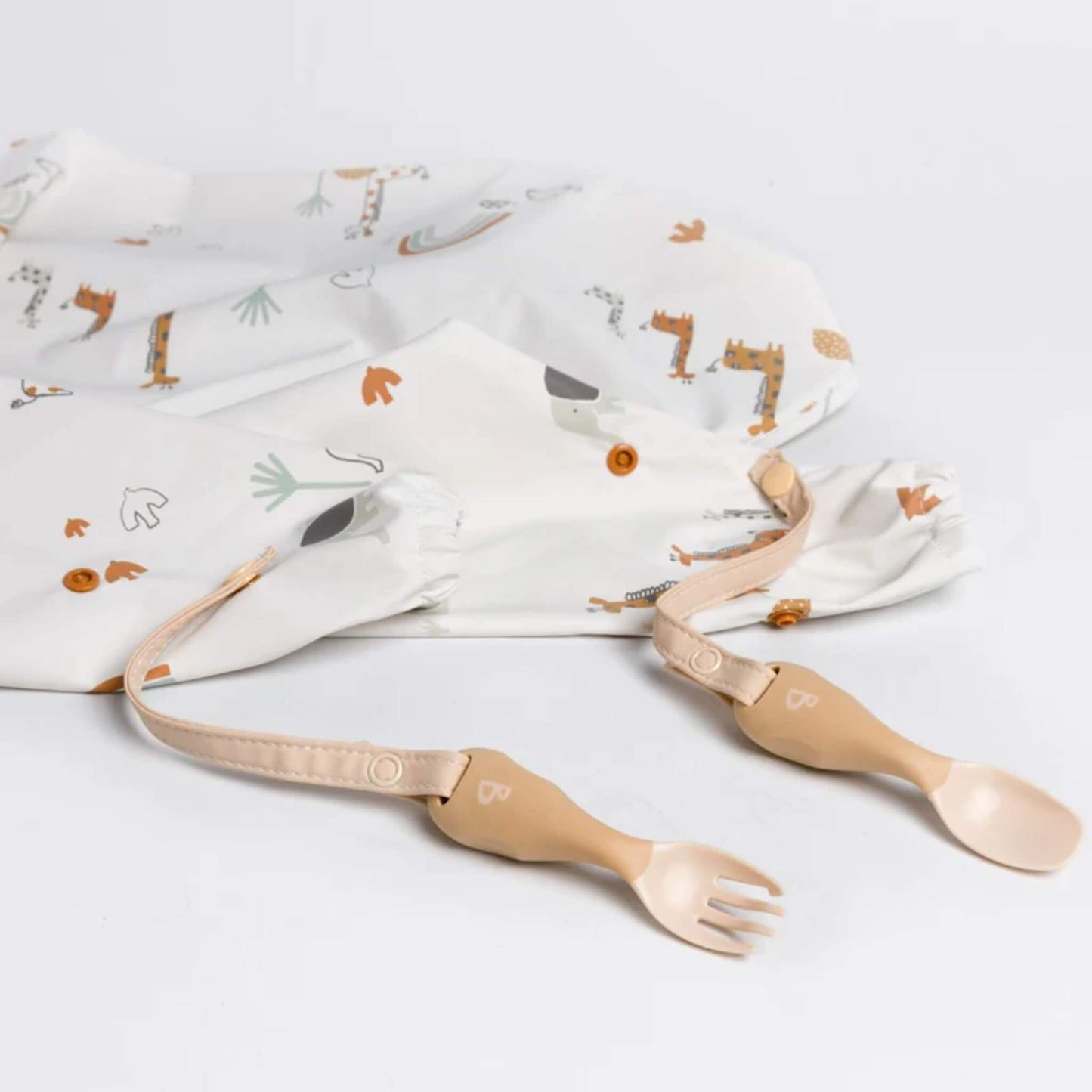 Neutral-toned toddler cutlery set clipped to a safari animal-print coverall bib, displayed on a white surface.
