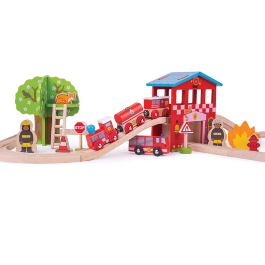 Wooden fire engine train climbs over the bridge near a fire station, with a fire engine truck, firefighters, stop sign, flame and rescue scene details around the track.