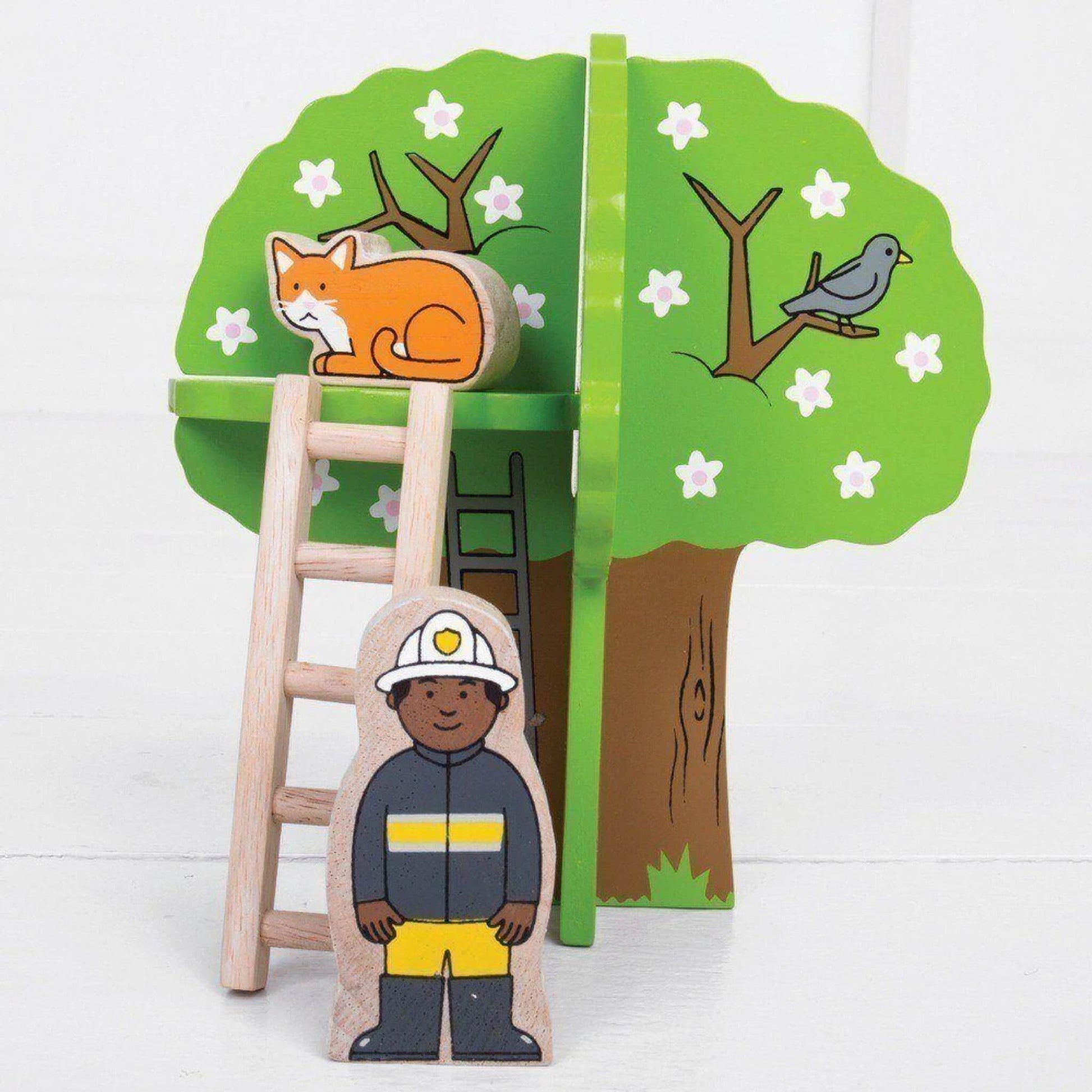Wooden firefighter figure stands next to a ladder propped against a leafy green tree with a painted bird and a removable wooden cat figure perched on top.