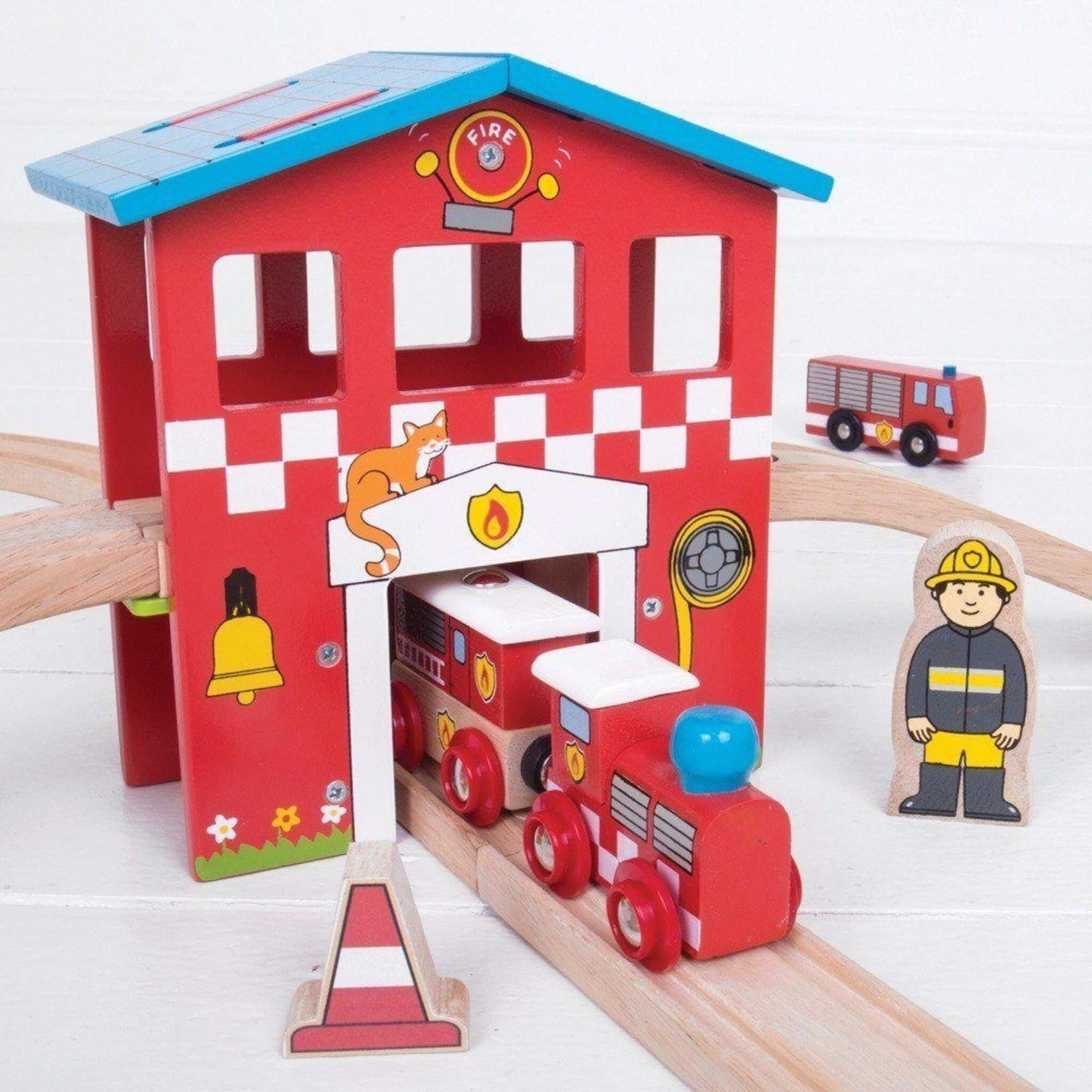 Bright red wooden fire station with illustrated firefighter details and a train engine exiting the station doors underneath a raised track.