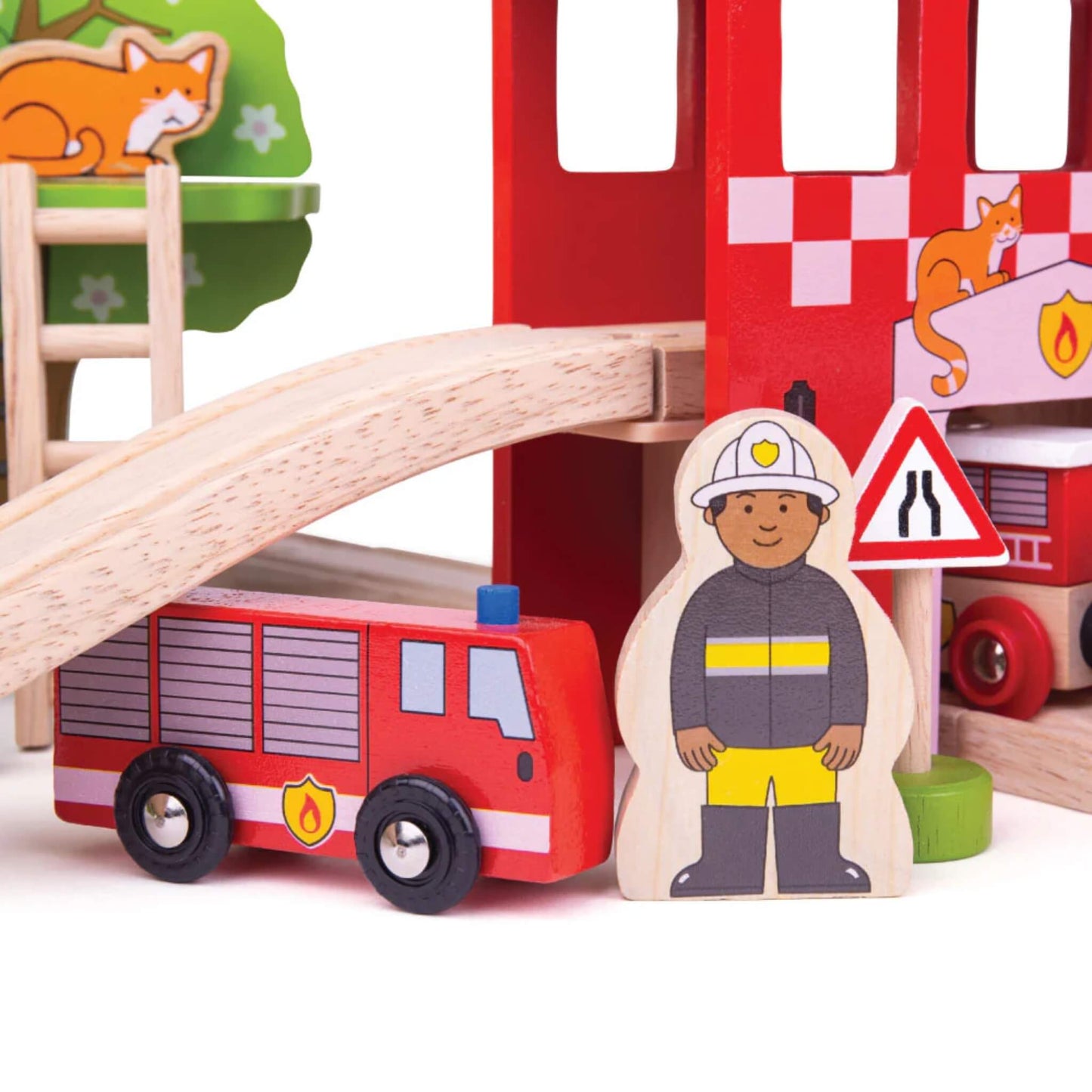 Wooden firefighter figure and fire truck parked beneath the bridge, next to a narrowing road sign and the corner of the fire station wall.