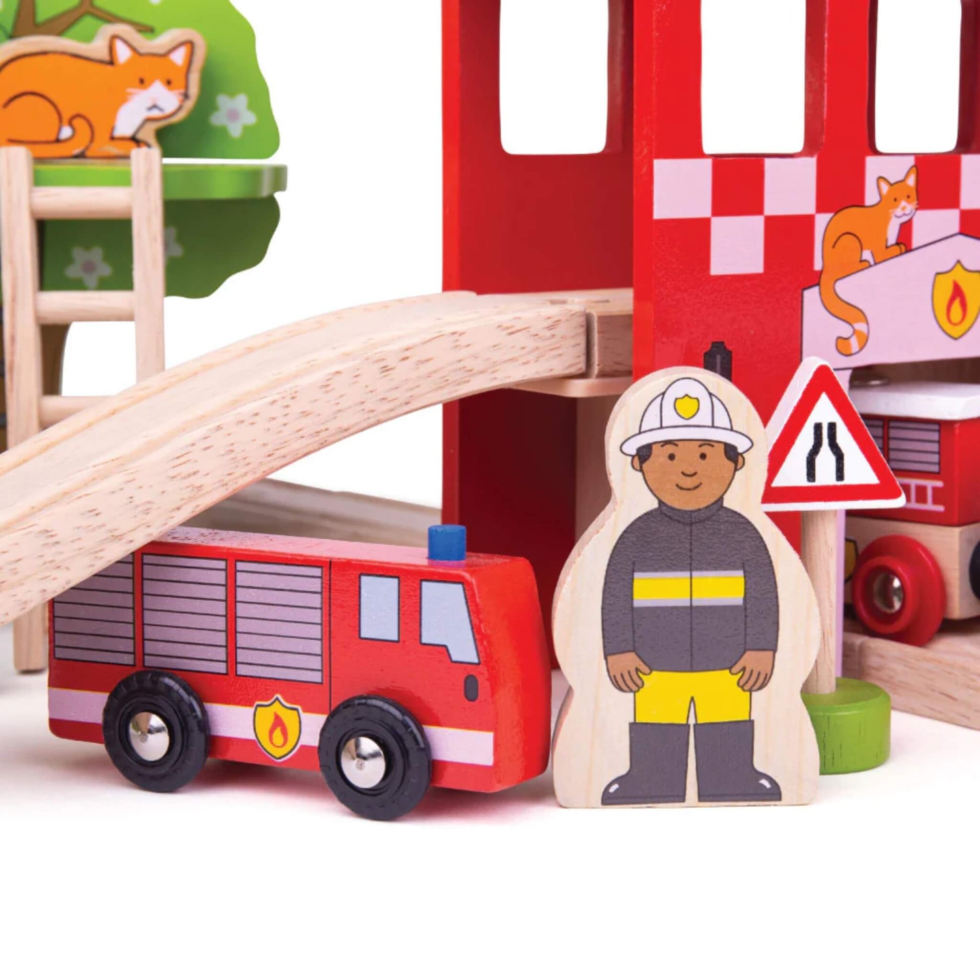 Wooden firefighter figure and fire truck parked beneath the bridge, next to a narrowing road sign and the corner of the fire station wall.