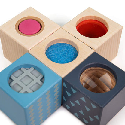 A flat lay of five sensory blocks, each showing a different feature including scratchy felt, soft rubber, and reflective prisms.