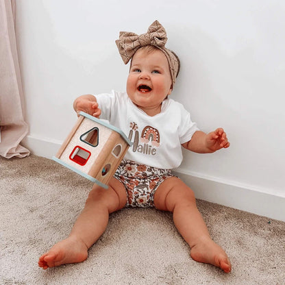 Toddler holding up the Bigjigs Shape Sorter with a playful expression, surrounded by shapes.