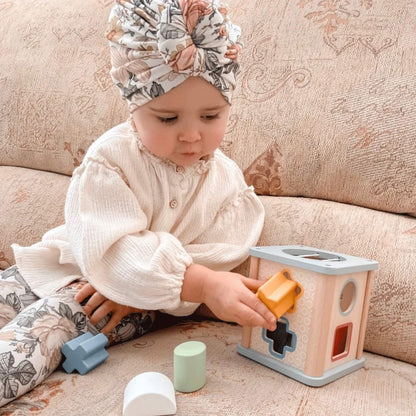 Child seated on a sofa, placing the yellow star into the Bigjigs Shape Sorter.