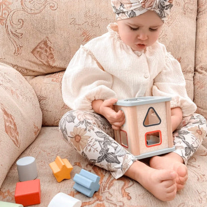 Toddler inspecting the Bigjigs Shape Sorter with assorted shapes laid out on a patterned sofa.
