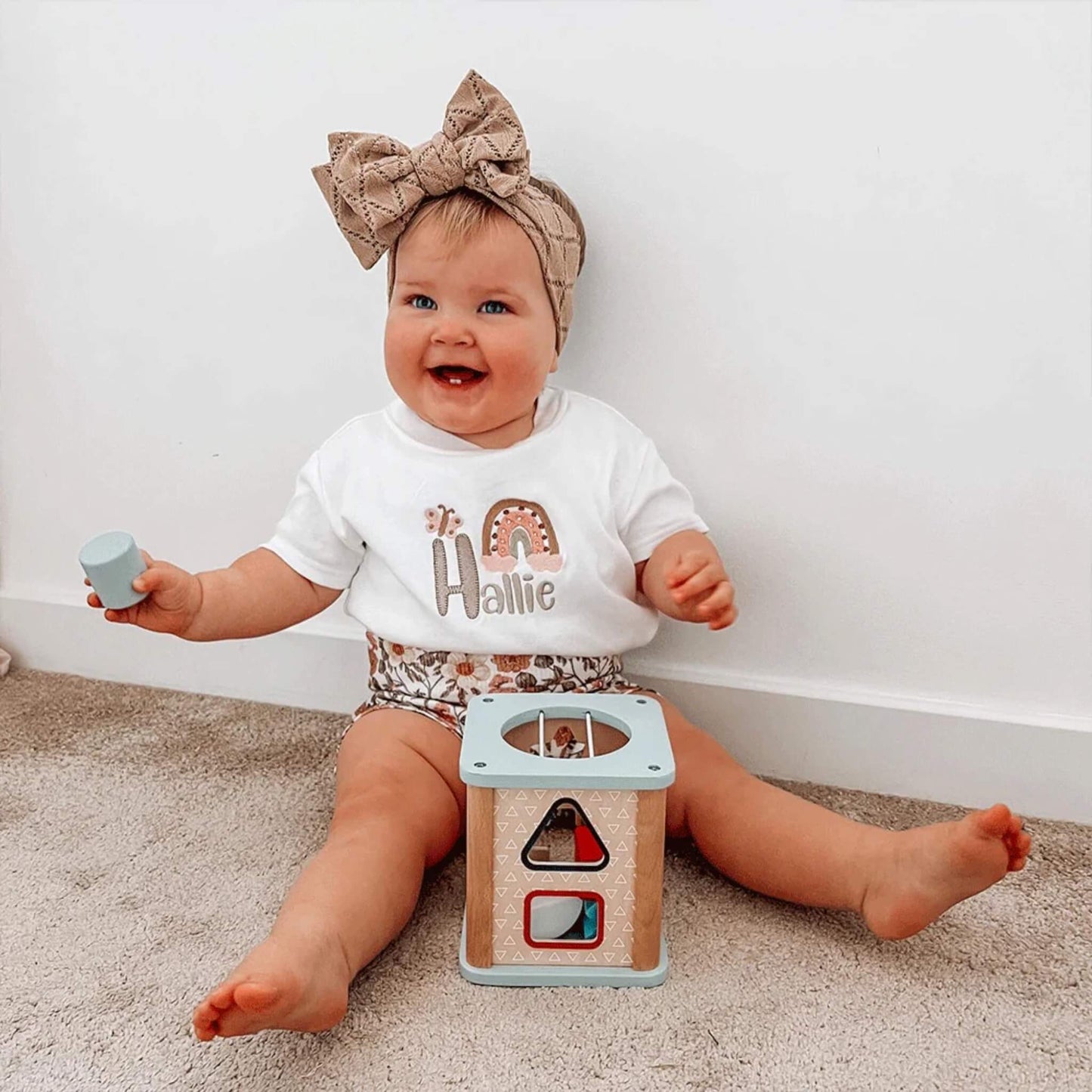 Smiling toddler playing with the Bigjigs Shape Sorter while holding a blue shape.
