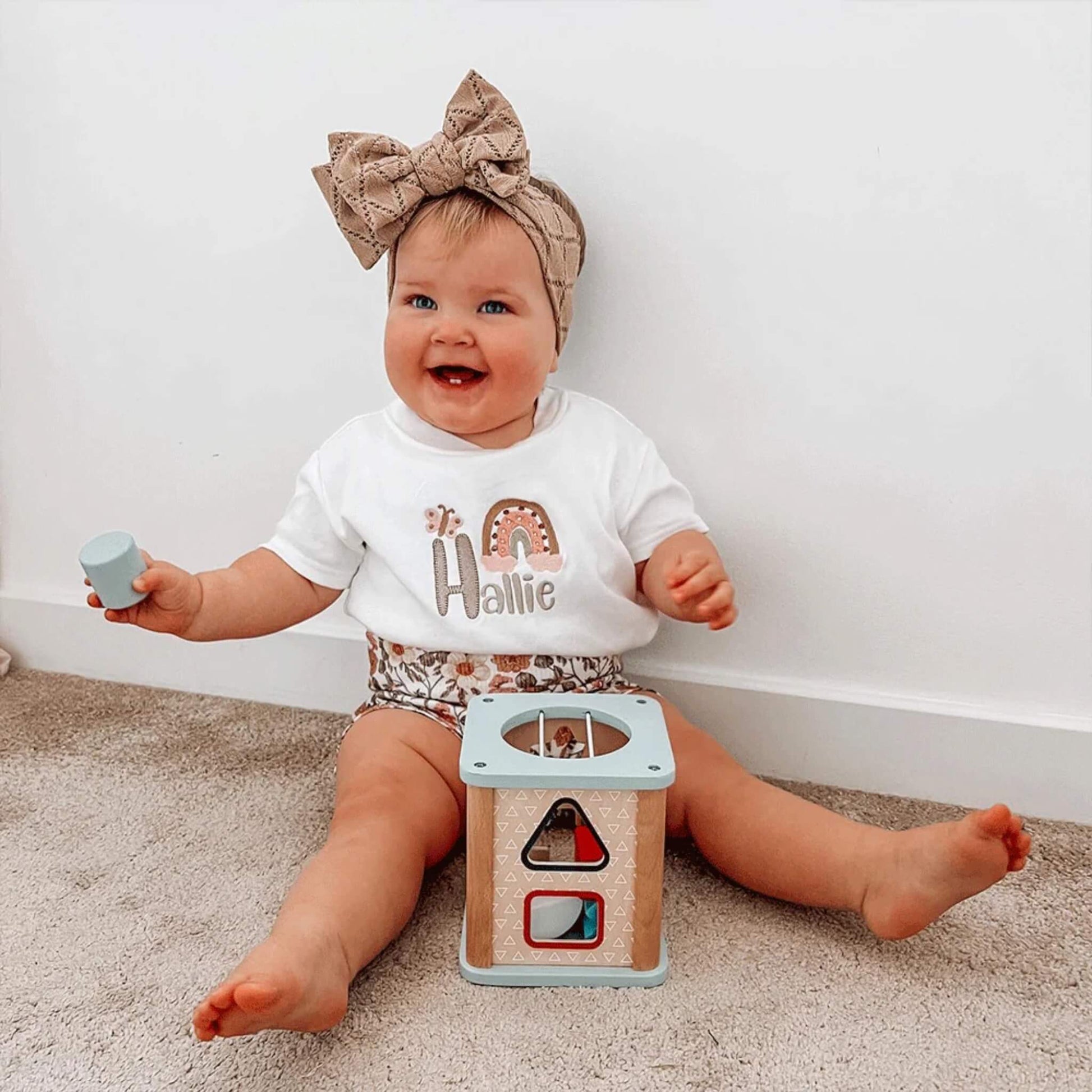 Smiling toddler playing with the Bigjigs Shape Sorter while holding a blue shape.