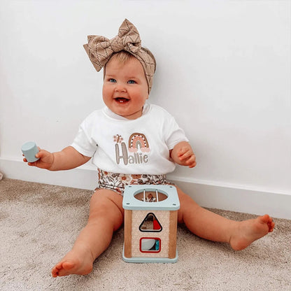 Smiling toddler playing with the Bigjigs Shape Sorter while holding a blue shape.