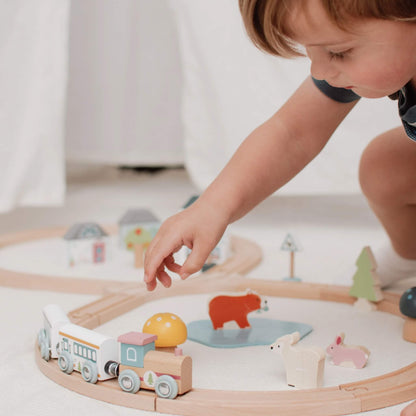A young child gently placing a train carriage on the wooden track, surrounded by colourful woodland animals and scenery.