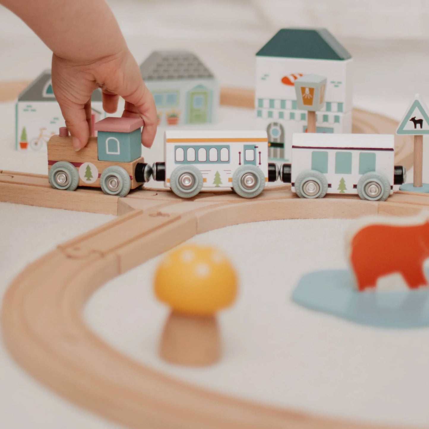 A close-up of a child’s hand pushing the eco-style train engine around the curved wooden railway track.