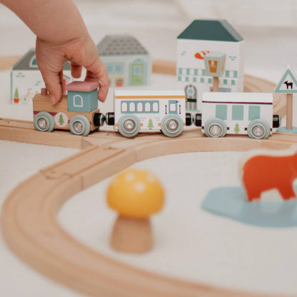 A close-up of a child’s hand pushing the eco-style train engine around the curved wooden railway track.