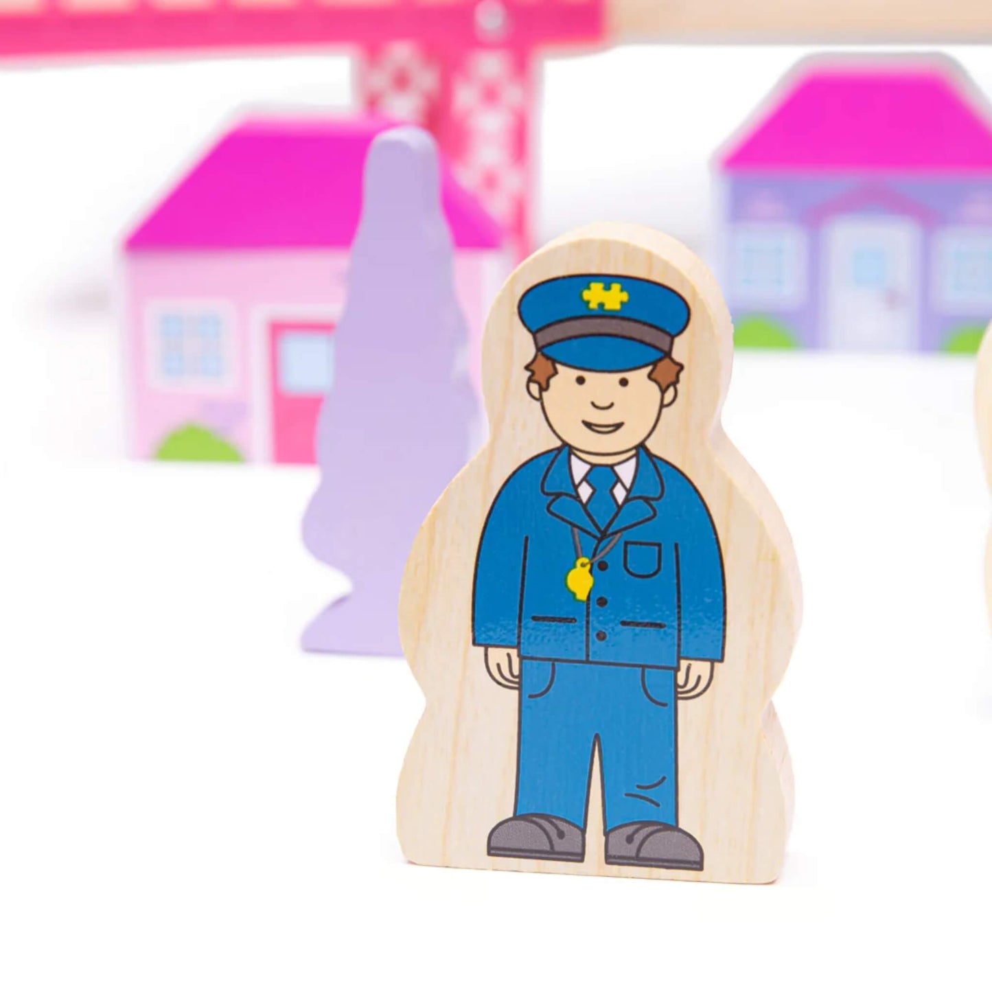 Wooden train conductor figure in blue uniform from the Bigjigs Fairy Town Train Set, with pink houses and lilac trees in the background.