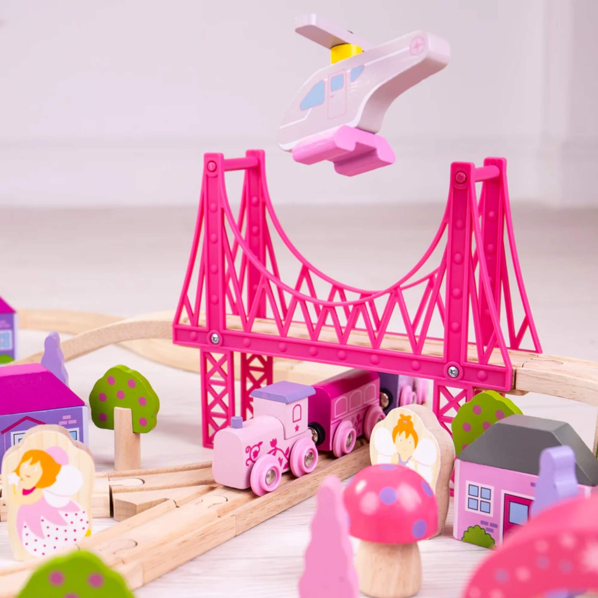 Flying fairy helicopter hovering above the pink train and bridge, with fairies, mushroom trees, and village buildings in the scene below.