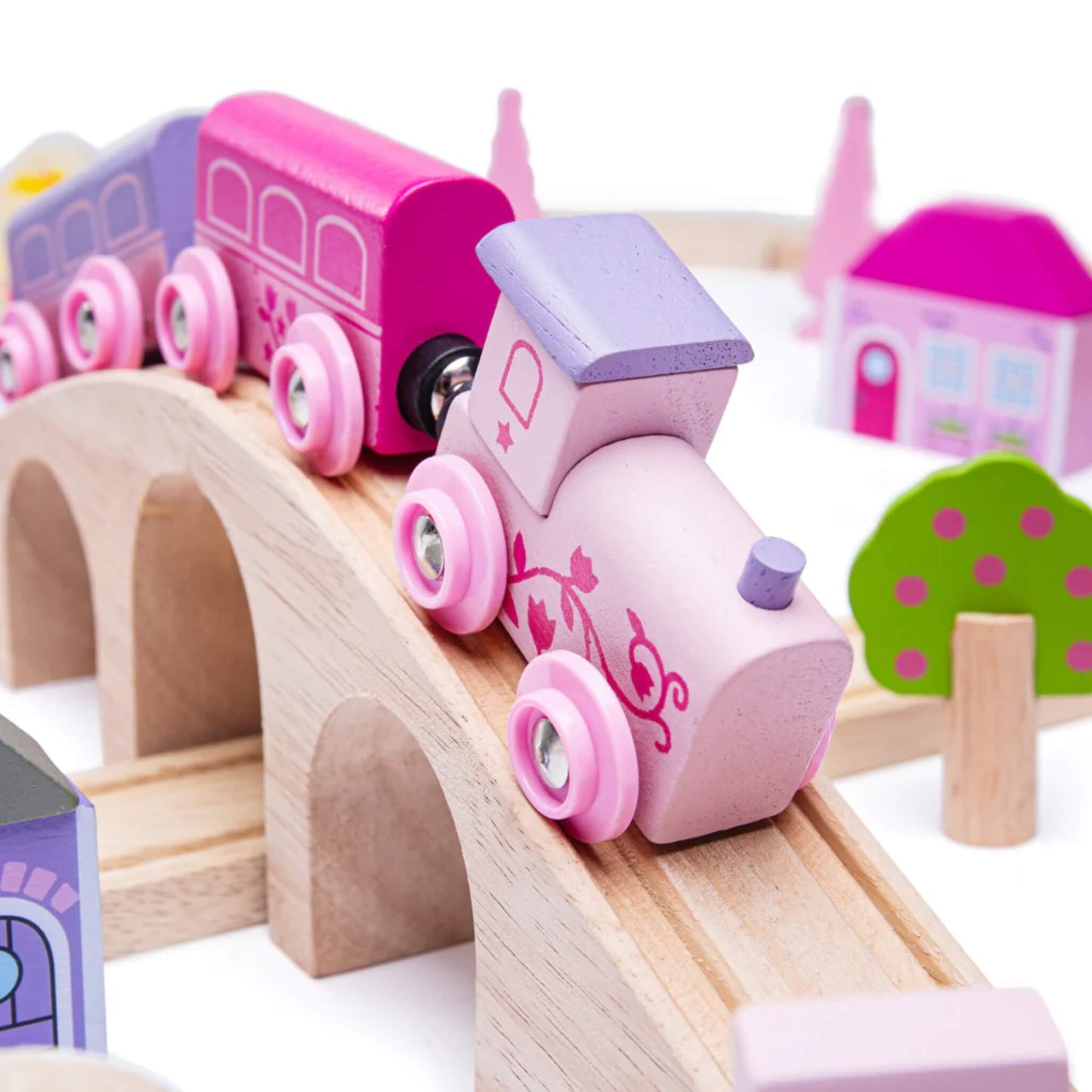 Close-up of the pink wooden fairy engine with matching carriages climbing a curved wooden bridge, decorated with floral designs.