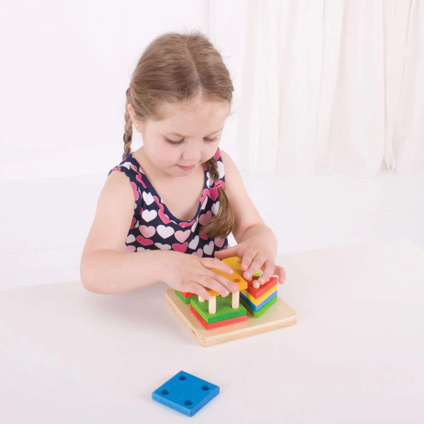 Young child concentrating as they stack and sort the brightly coloured wooden pieces on the pegged baseboard – building fine motor skills.