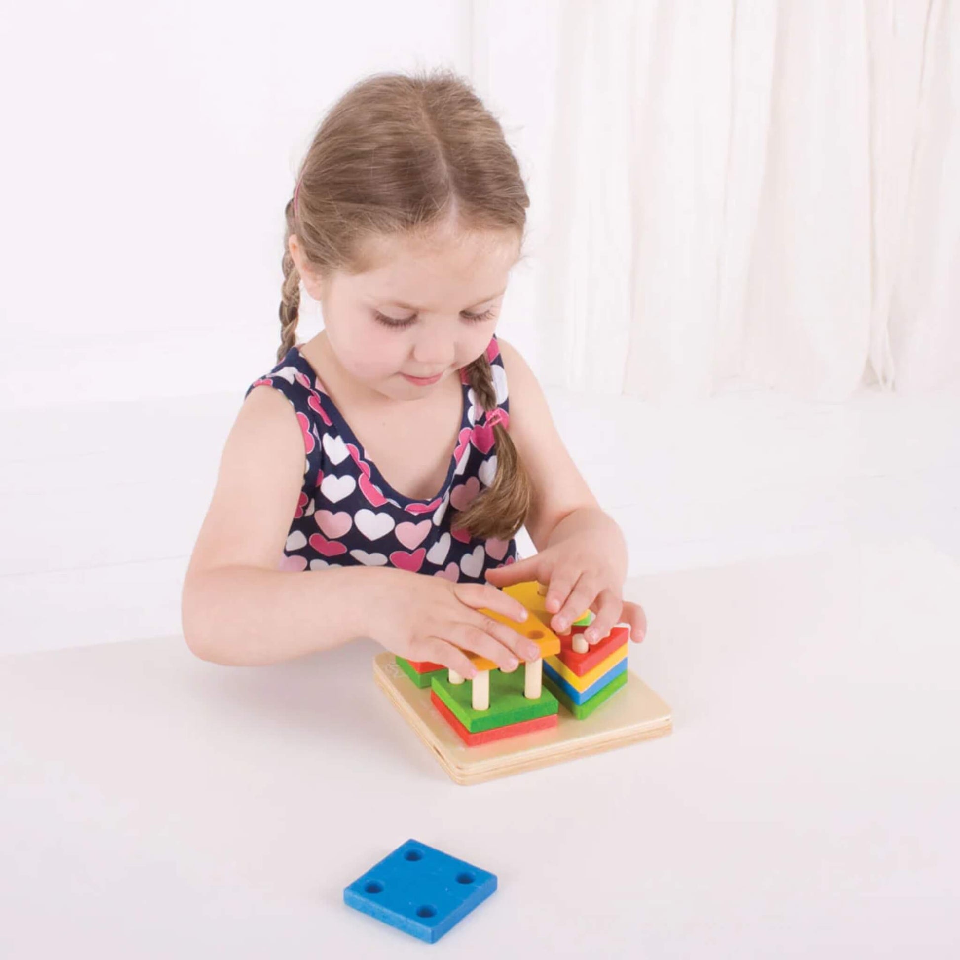 Young child concentrating as they stack and sort the brightly coloured wooden pieces on the pegged baseboard – building fine motor skills.