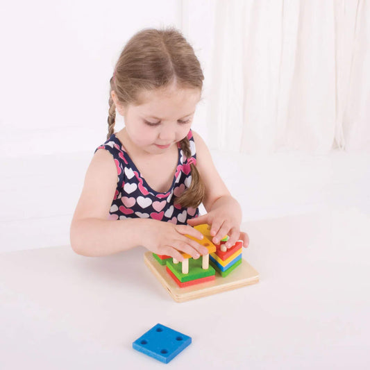 Young child concentrating as they stack and sort the brightly coloured wooden pieces on the pegged baseboard – building fine motor skills.