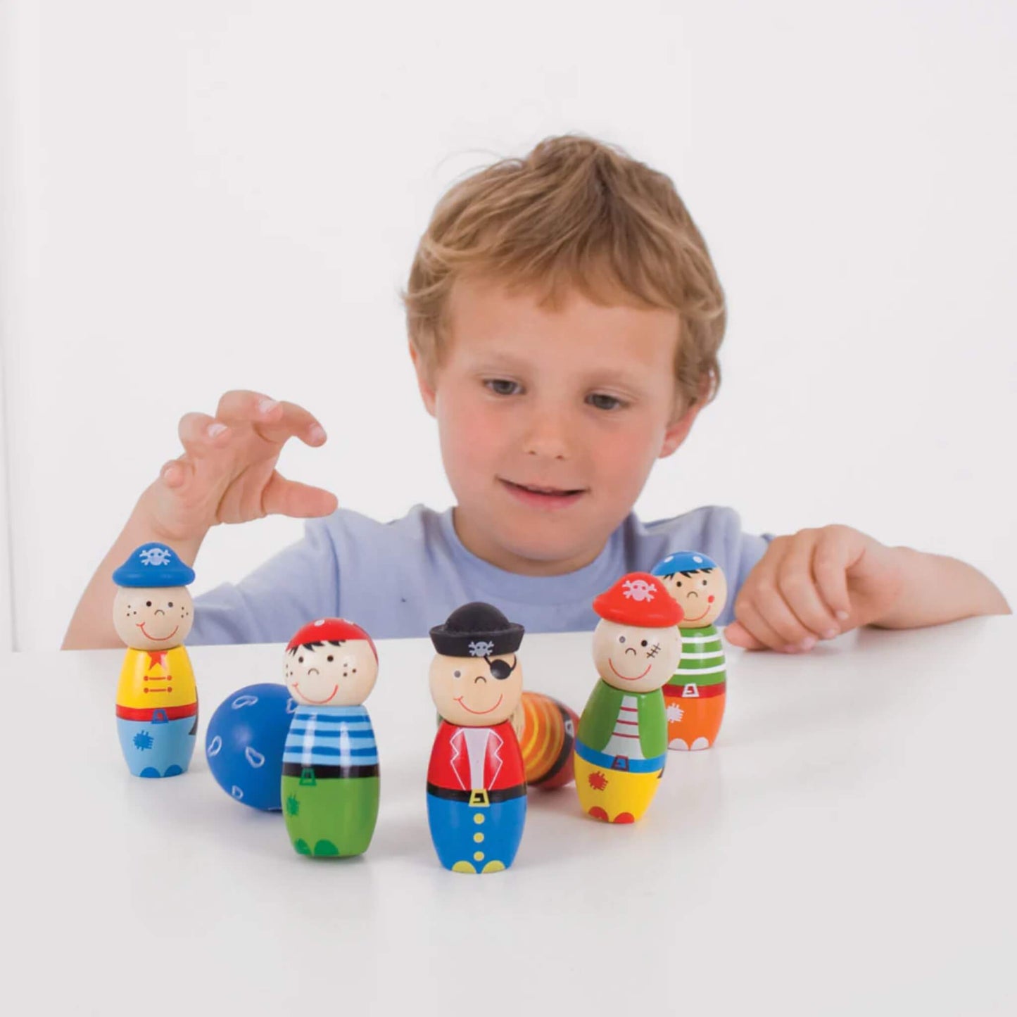 Young child smiling and playing with the Bigjigs pirate skittles set, reaching to set them up again.
