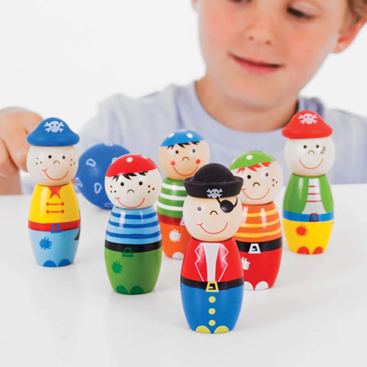 Child playing with six colourful pirate skittles, smiling as they aim the blue bowling ball at the characters.