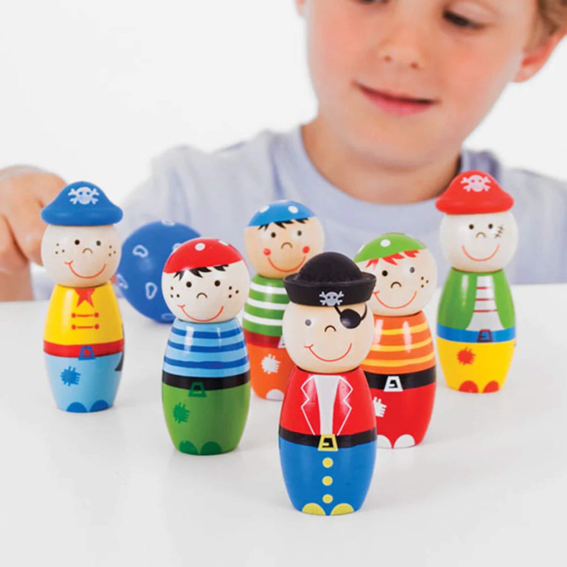 Child playing with six colourful pirate skittles, smiling as they aim the blue bowling ball at the characters.