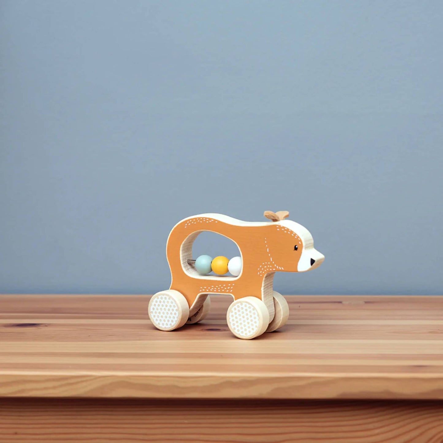 The Push Along Bear toy positioned on a wooden surface with a soft blue background, showing off its smooth shape and natural textures.
