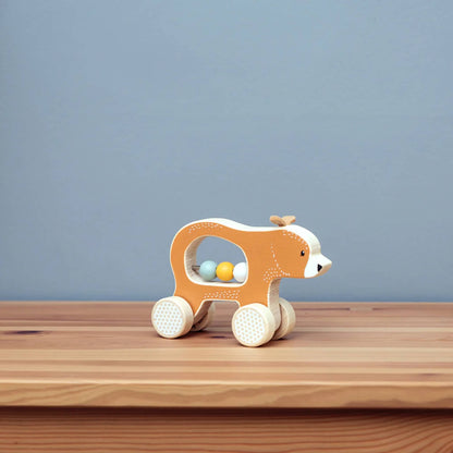 The Push Along Bear toy positioned on a wooden surface with a soft blue background, showing off its smooth shape and natural textures.