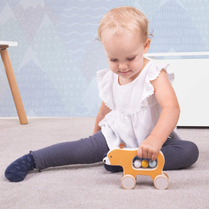 A toddler sitting on the floor playing with the Push Along Bear, holding it by the centre cut-out for easy movement and tactile exploration.
