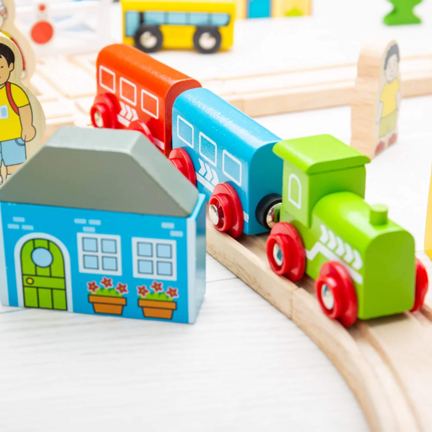 Close-up of the green engine and two colourful carriages from the Bigjigs Toys Town & Country Train Set travelling past a blue wooden house.