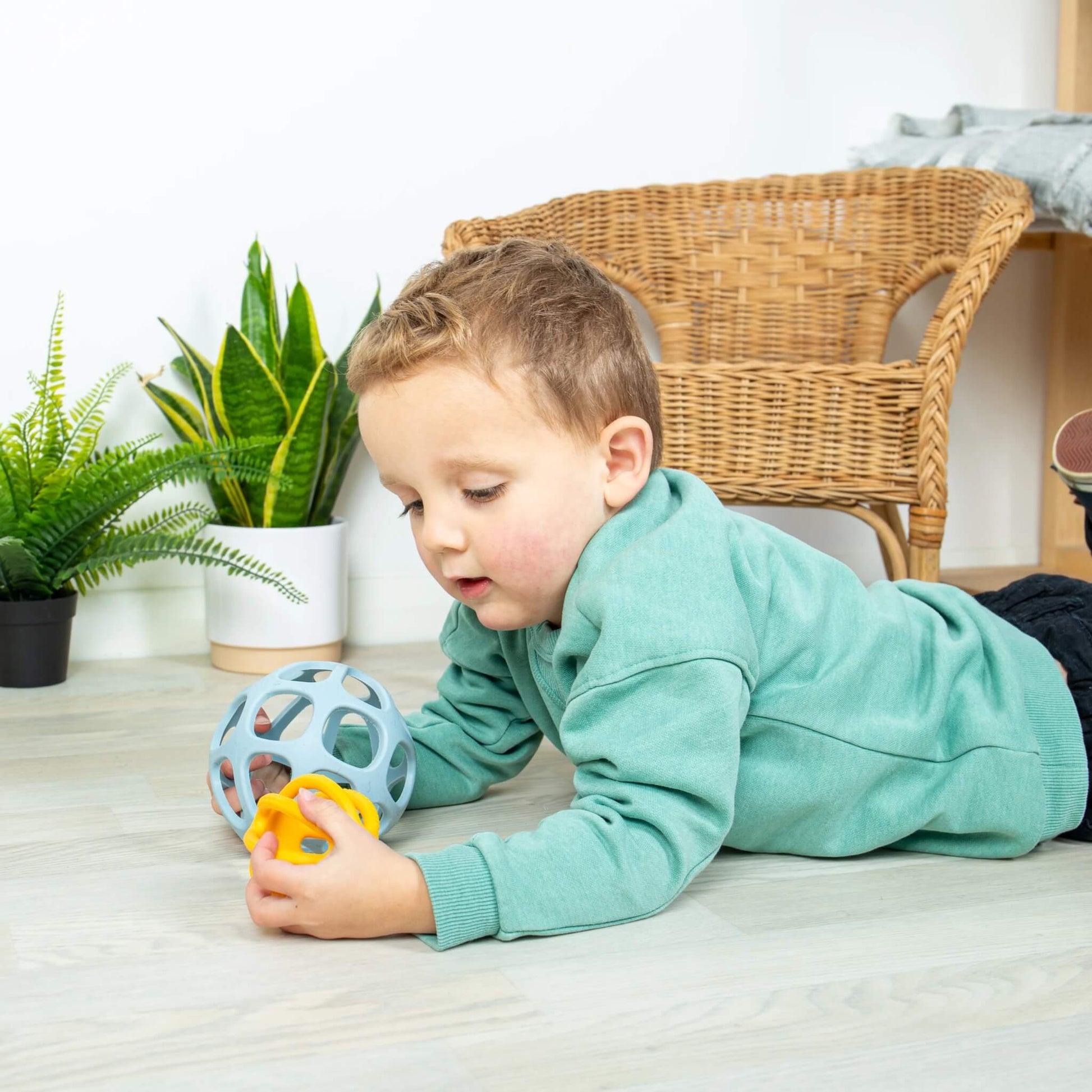 Toddler lying on the floor playing with the Bigjigs Toys Activity Balls, exploring the nesting and tactile features.