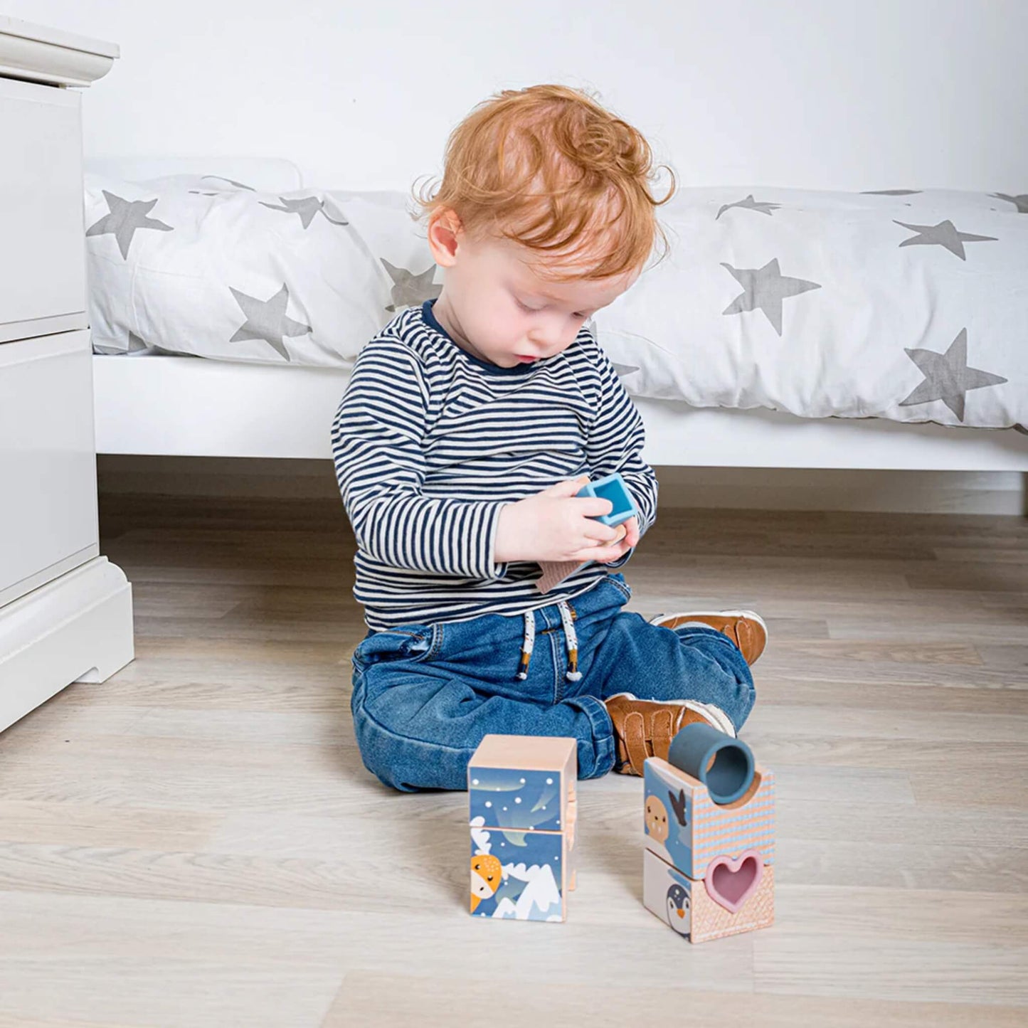 Toddler arranging Arctic-themed stacking blocks on a wooden floor, exploring shapes and balance.