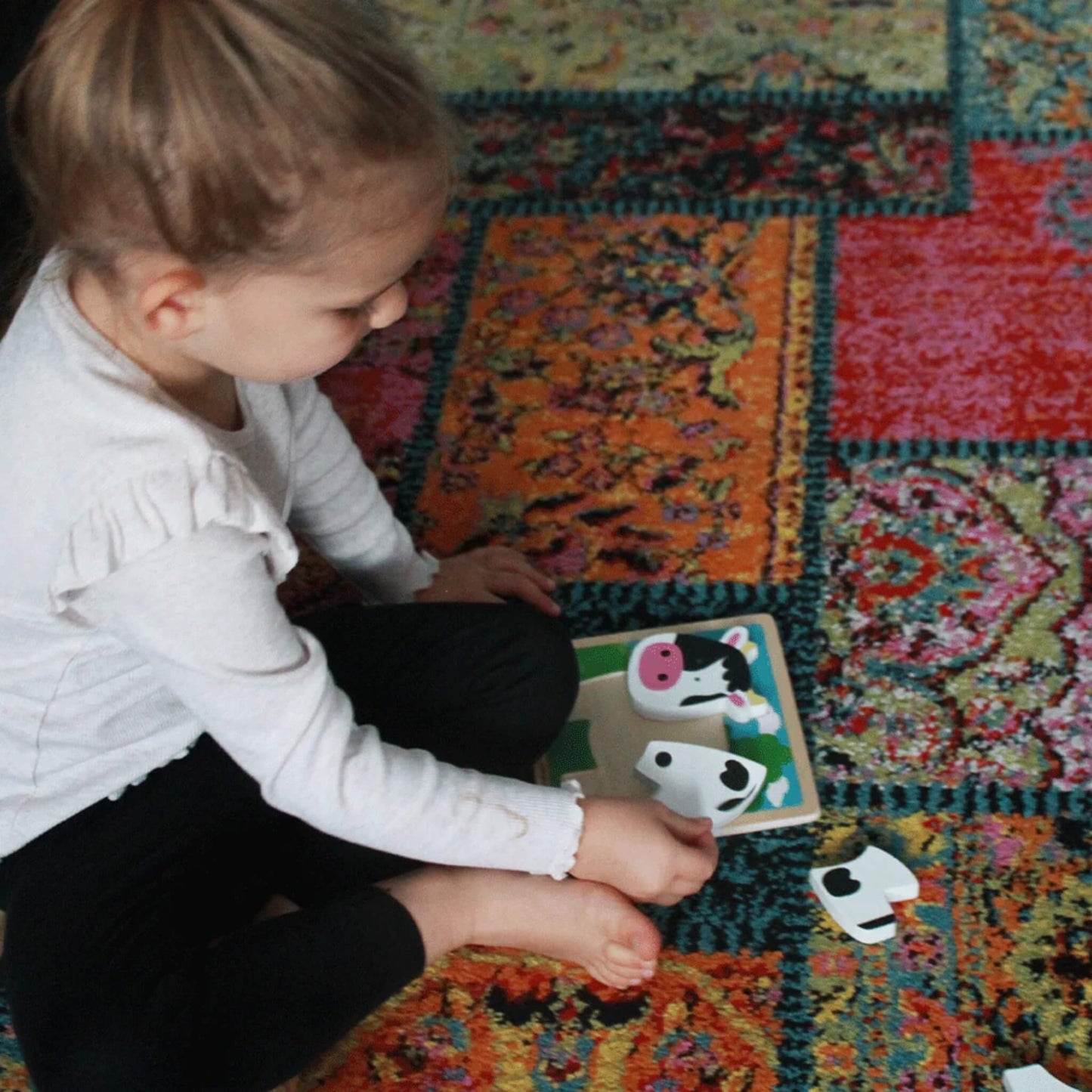 A toddler carefully placing chunky cow puzzle pieces on a sturdy wooden base, exploring shapes and colours.