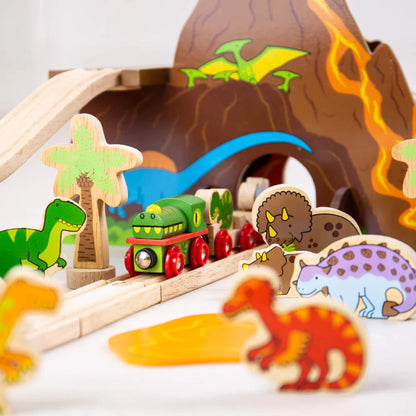 Dinosaur-themed green train emerging from the volcano tunnel, surrounded by wooden dinosaur characters and palm trees in a prehistoric scene.