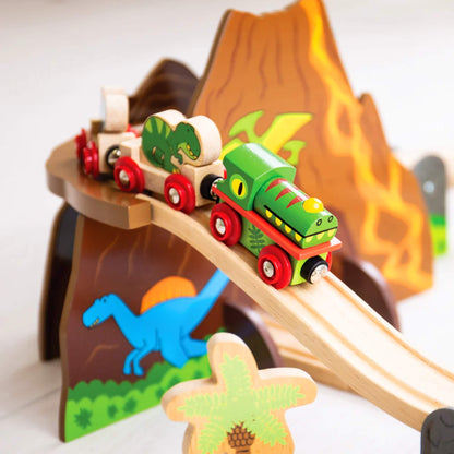 Elevated track section with the green dinosaur train climbing above the volcano tunnel, with colourful prehistoric designs and wooden characters below.